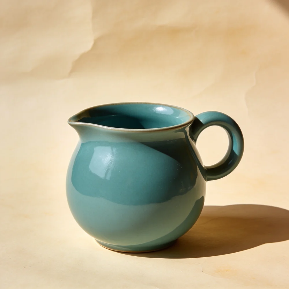 Rounded-belly ceramic mug with pinched lip, rounded loop handle and glossy teal glaze