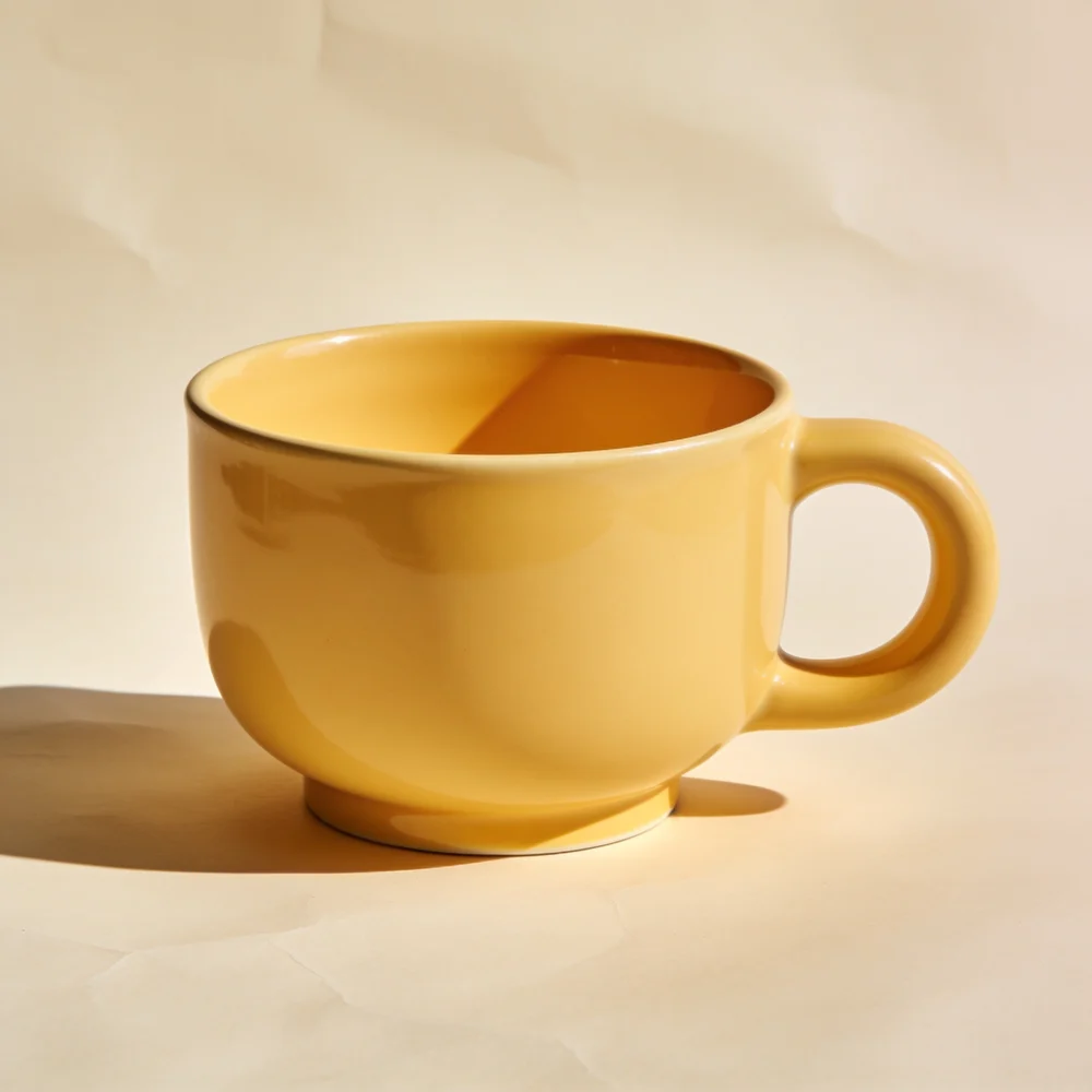 Wide low ceramic breakfast bowl-shaped mug with broad low loop handle, warm butter yellow glaze
